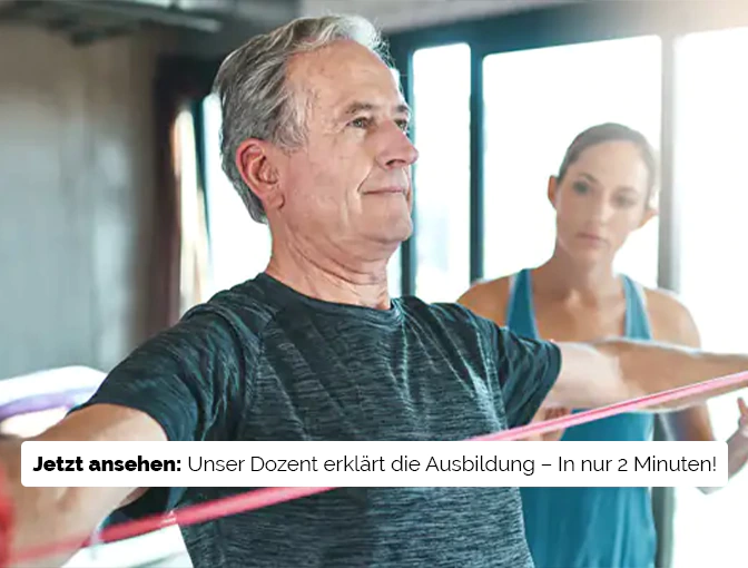 Eine Sport- und Gesundheitstrainerin beobachtet und korrigiert einen älteren Mann bei der Ausführung einer Therabandübung.