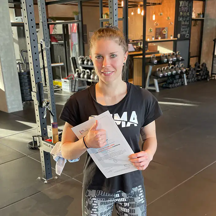 OTL Zertifikat Kundin Daniela hält ihr Athletiktrainer-Zertifikat in den Händen und hebt ihren Daumen.