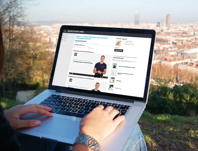 Foto einer Person, die in der Natur mit ihrem Laptop sitzt und Inhalte der Ausbildung zum Sport- und Gesundheitstrainer im Online Campus lernt